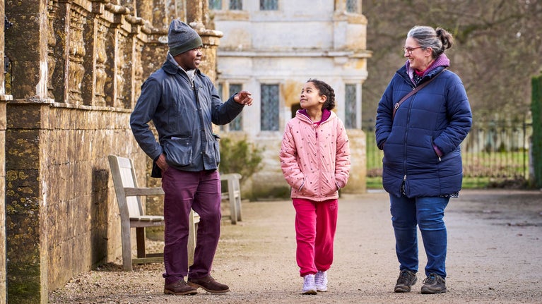 A family of three talking and walking past a balustraded wall at Montacute House